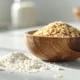 un bol de madera con avena en su interior. Alrededor de la mesa fibra de avena y avena.
